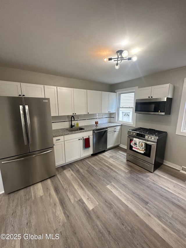 kitchen with appliances with stainless steel finishes, a sink, white cabinets, and light wood finished floors