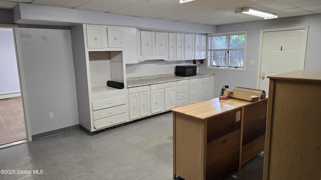 505 Elm Ave, Bethlehem, NY 12158 - kitchen with white cabinetry, black microwave, a paneled ceiling, a baseboard heating unit, and baseboards