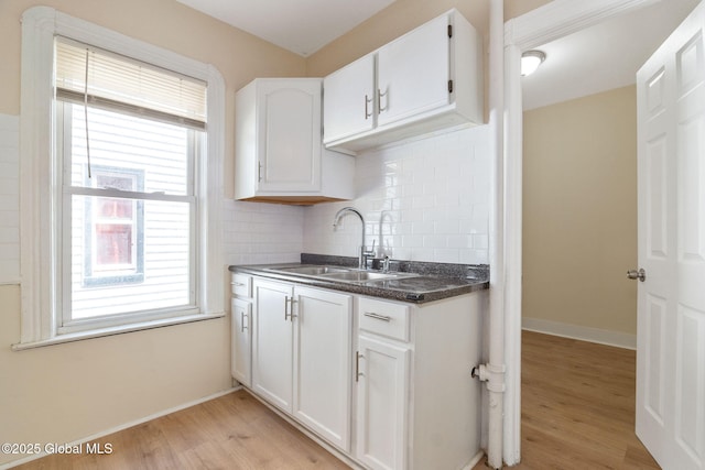 kitchen featuring a sink, dark countertops, light wood finished floors, tasteful backsplash, and white cabinetry