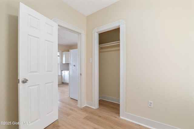 unfurnished bedroom with light wood finished floors, freestanding refrigerator, baseboards, and a closet