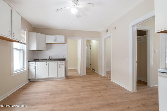 kitchen with ceiling fan, white cabinetry, decorative backsplash, light wood finished floors, and baseboards