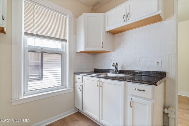 kitchen with a sink, decorative backsplash, baseboards, and light wood-style flooring
