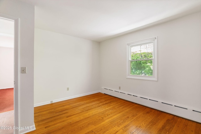 empty room featuring a baseboard radiator, light wood-style floors, and baseboards