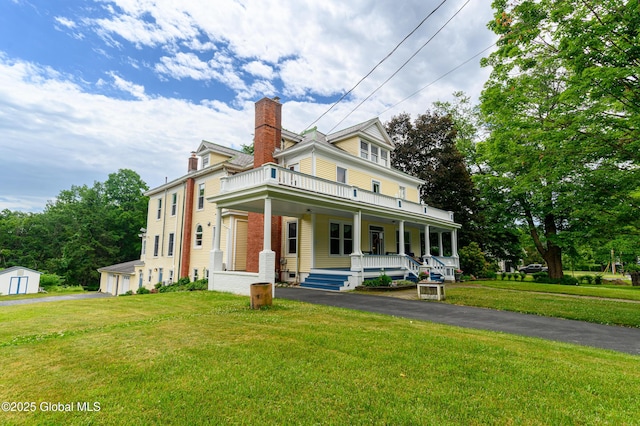 view of front of home with a porch, a chimney, a front yard, a shed, and an outbuilding
