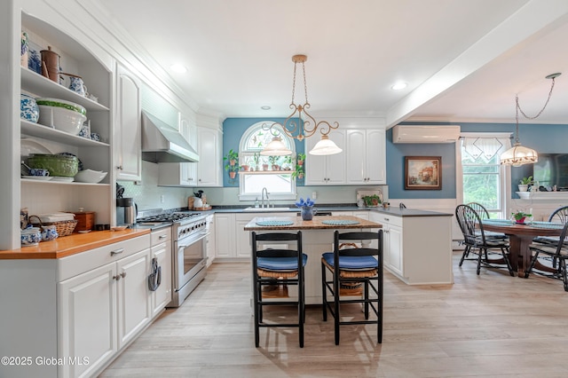 kitchen featuring stainless steel range, wall chimney range hood, a wall mounted AC, plenty of natural light, and crown molding