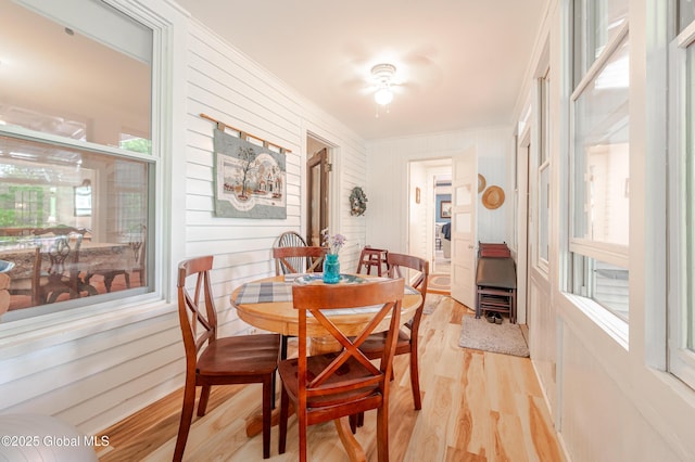dining room featuring light wood finished floors, a wood stove, ornamental molding, wooden walls, and ceiling fan