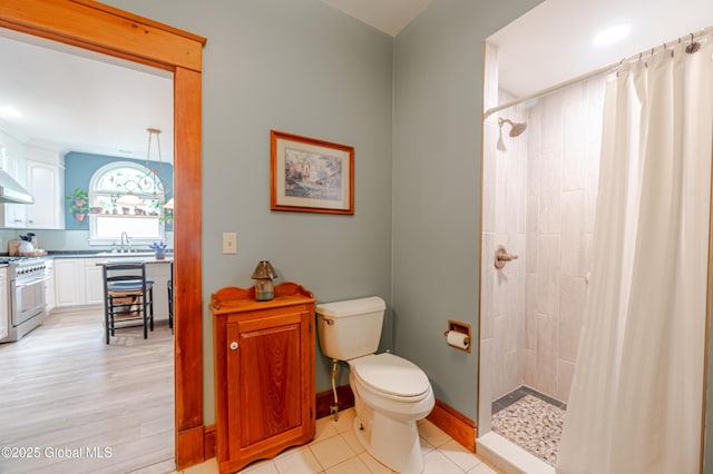 full bathroom with a sink, a tile shower, toilet, and baseboards