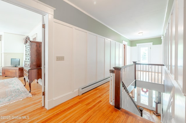 hall with an upstairs landing, a baseboard radiator, light wood finished floors, ornamental molding, and a decorative wall