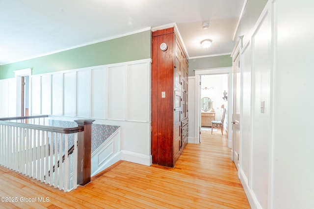 hall featuring light wood-style flooring, crown molding, and an upstairs landing