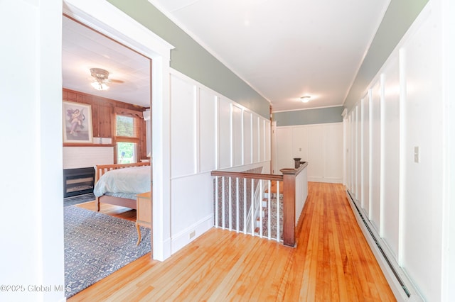 corridor with baseboard heating, an upstairs landing, light wood-style floors, and a decorative wall