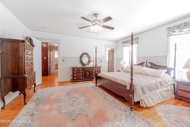 bedroom with wainscoting, wood finished floors, ceiling fan, and a decorative wall