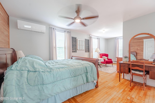 bedroom featuring a wall mounted AC, light wood finished floors, and a ceiling fan