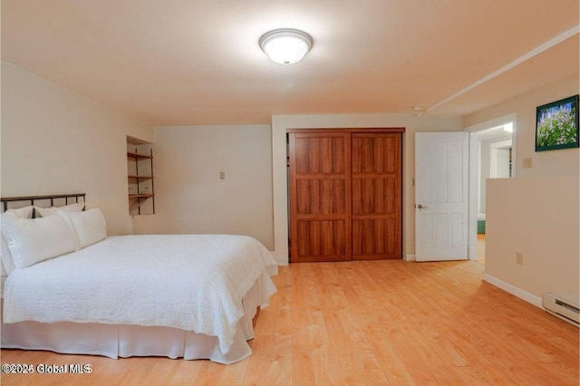 bedroom with light wood finished floors, baseboard heating, and baseboards