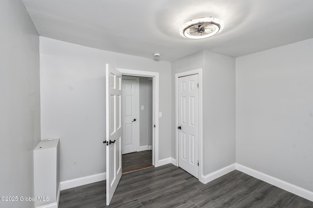 unfurnished bedroom with dark wood-style floors, baseboards, and a closet