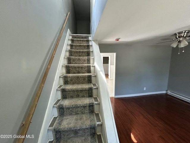 stairway with ceiling fan, wood finished floors, baseboards, and a baseboard heating unit