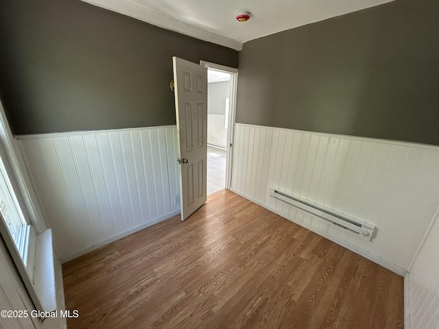 empty room with a baseboard heating unit, wainscoting, wood finished floors, and baseboard heating