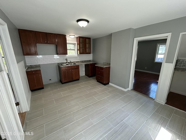 kitchen featuring decorative backsplash, a sink, glass insert cabinets, baseboards, and light countertops