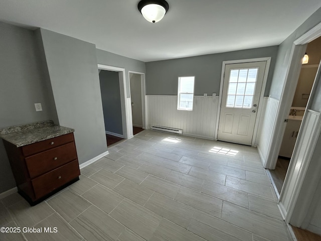 unfurnished dining area featuring a baseboard heating unit and a wainscoted wall