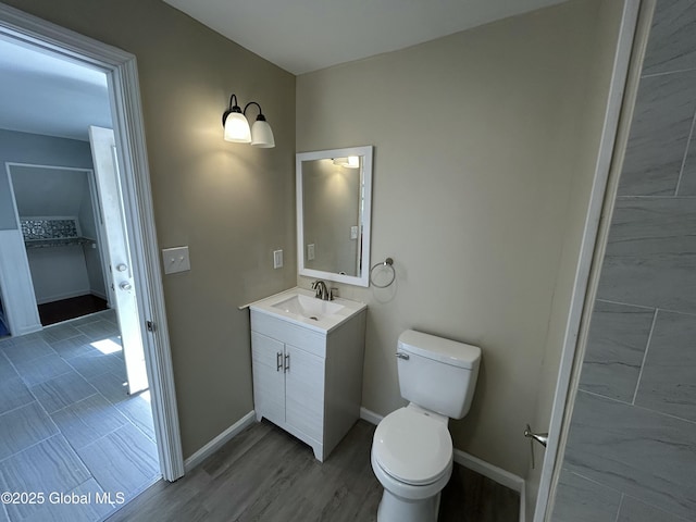 bathroom with wood finished floors, vanity, toilet, and baseboards