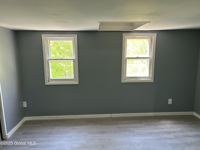 spare room featuring wood finished floors, baseboards, and attic access