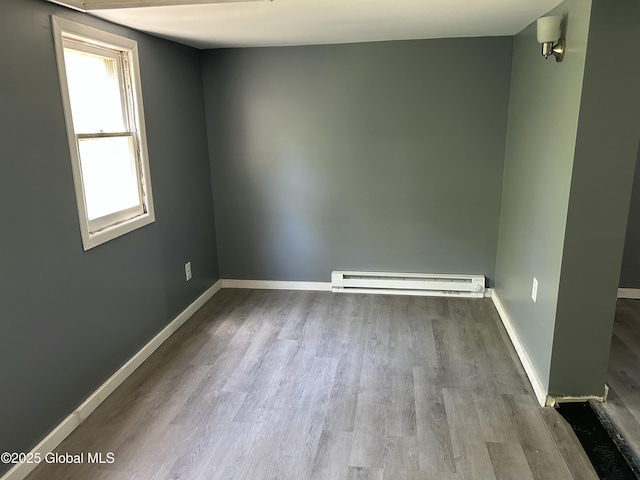 empty room with baseboard heating, wood finished floors, and baseboards