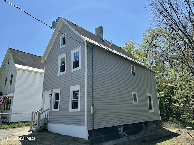 view of home's exterior with entry steps, a chimney, and fence
