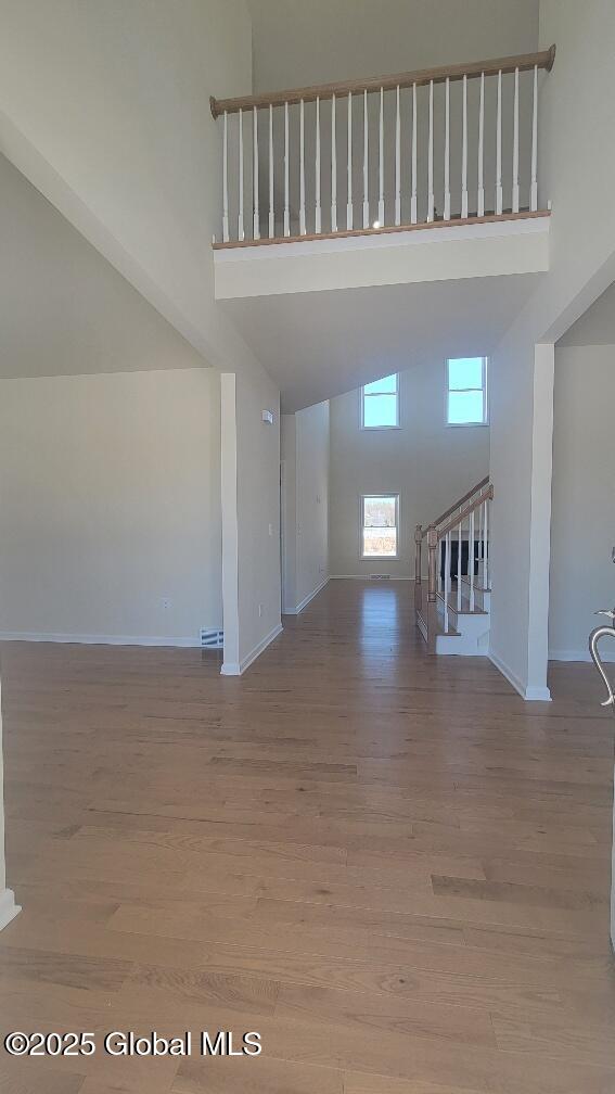35 Sally St, Halfmoon, NY 12118 - unfurnished living room with high vaulted ceiling, baseboards, wood finished floors, and stairway