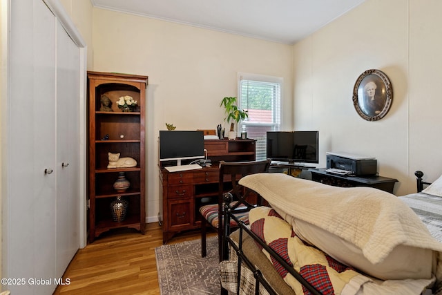 bedroom with light wood-style floors, crown molding, a desk, and a closet