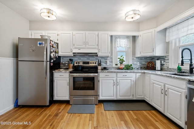 kitchen featuring appliances with stainless steel finishes, ventilation hood, a sink, white cabinets, and decorative backsplash