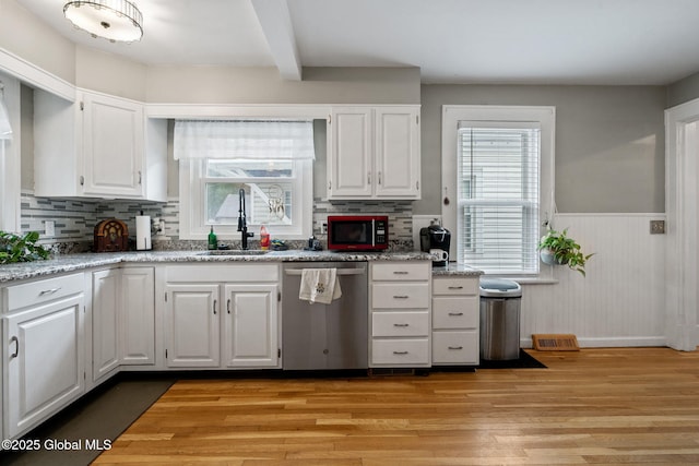kitchen with stainless steel dishwasher, a sink, a wainscoted wall, light wood-type flooring, and white cabinetry