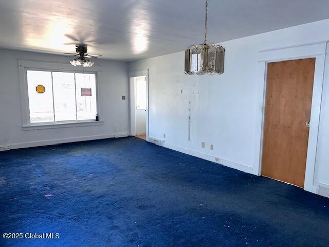 unfurnished dining area with carpet flooring, ceiling fan, a chandelier, and baseboards