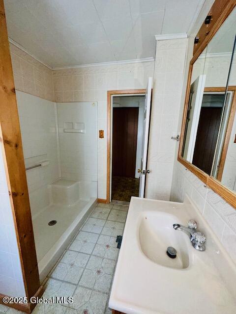 full bath featuring a sink, a shower stall, tile patterned floors, and crown molding