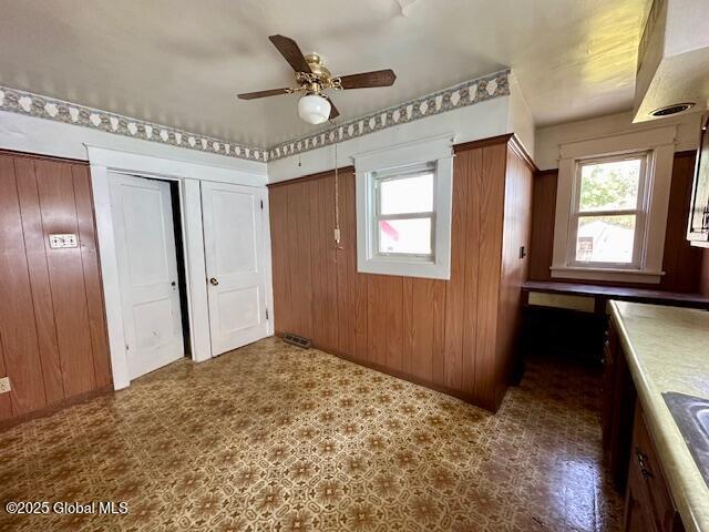 unfurnished bedroom with multiple windows, dark floors, wooden walls, and ceiling fan