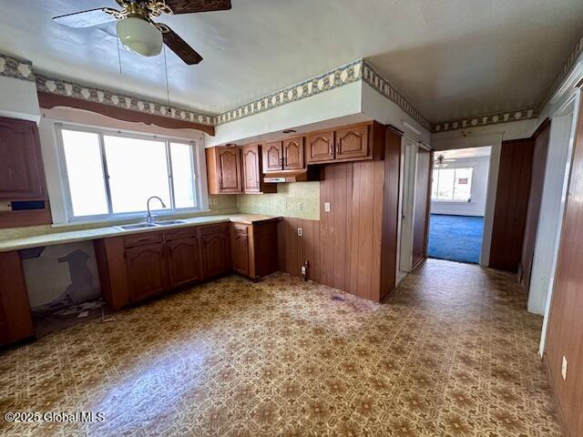 kitchen featuring a ceiling fan, healthy amount of natural light, a sink, brown cabinets, and wood walls