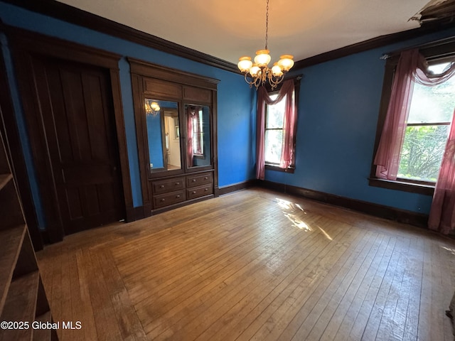 spare room featuring healthy amount of natural light, crown molding, a chandelier, hardwood / wood-style flooring, and baseboards
