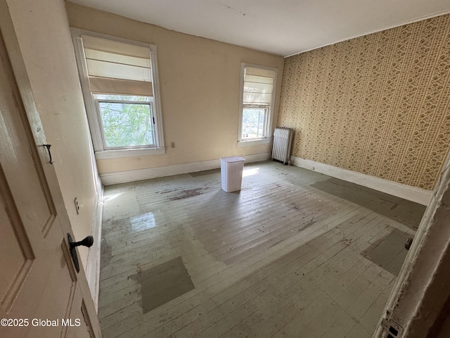 unfurnished room featuring radiator, plenty of natural light, baseboards, wallpapered walls, and wood-type flooring