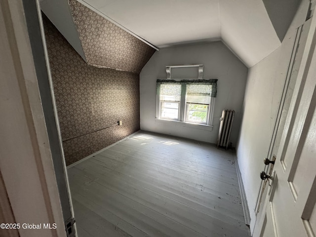 additional living space with radiator heating unit, wallpapered walls, hardwood / wood-style floors, and lofted ceiling