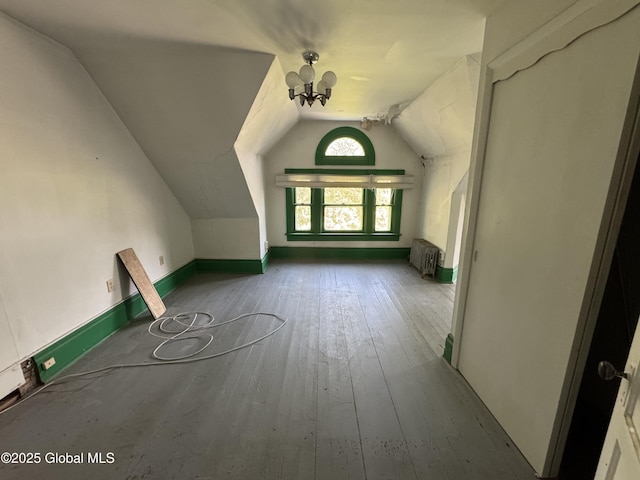 additional living space with vaulted ceiling, radiator, a chandelier, and wood-type flooring