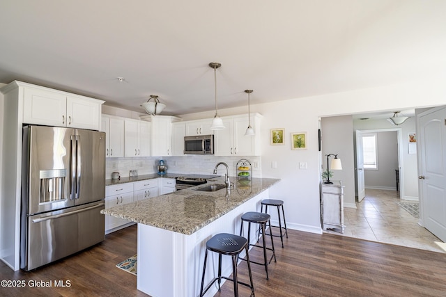 kitchen with stainless steel appliances, a sink, a peninsula, a kitchen breakfast bar, and light stone counters