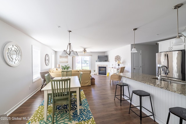 dining space with a glass covered fireplace, dark wood-style floors, ceiling fan, and baseboards