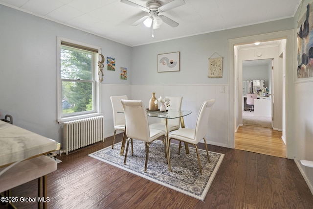 dining space featuring radiator heating unit, a ceiling fan, wood finished floors, crown molding, and wainscoting