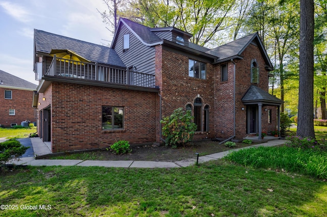 view of side of home featuring brick siding, a lawn, and a balcony