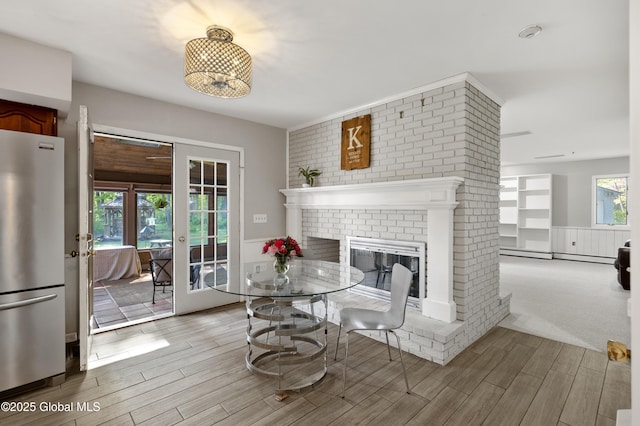 dining space featuring wood finished floors, a fireplace, a baseboard radiator, and french doors