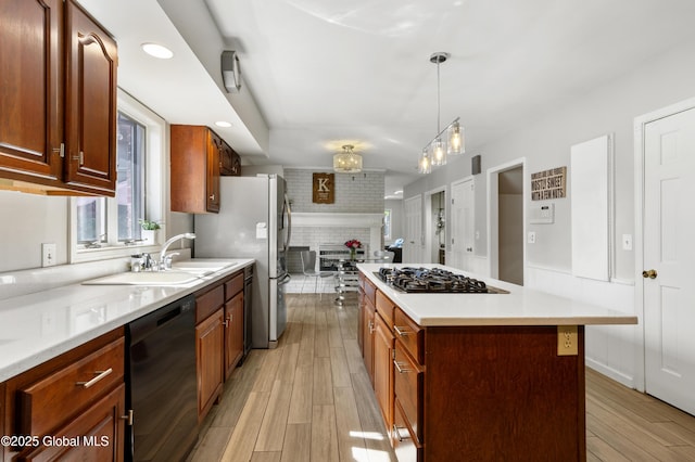 kitchen featuring appliances with stainless steel finishes, a sink, light wood finished floors, a center island, and light countertops