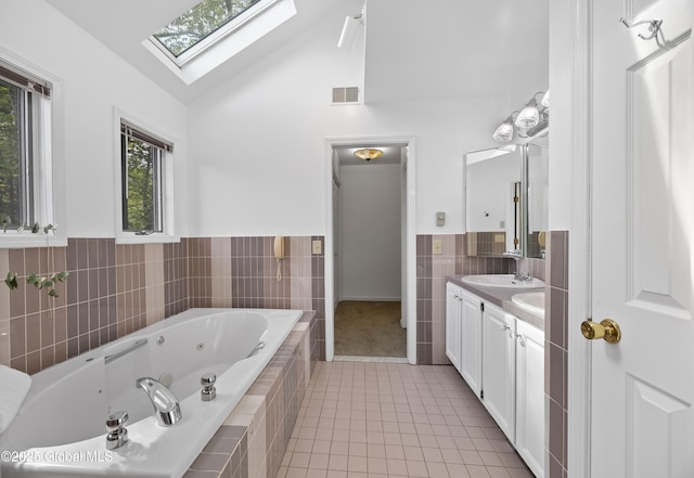 bathroom featuring tile walls, tile patterned floors, a skylight, vanity, and a whirlpool tub