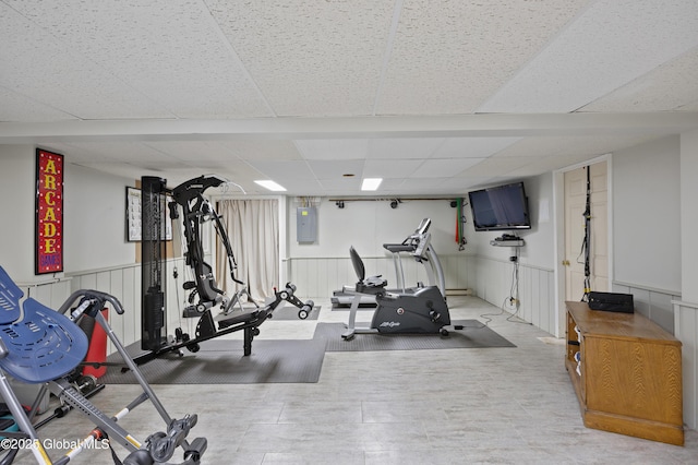 workout room featuring a paneled ceiling, electric panel, and a wainscoted wall