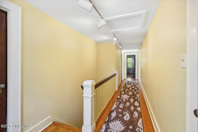 hallway with an upstairs landing, light wood finished floors, rail lighting, and baseboards