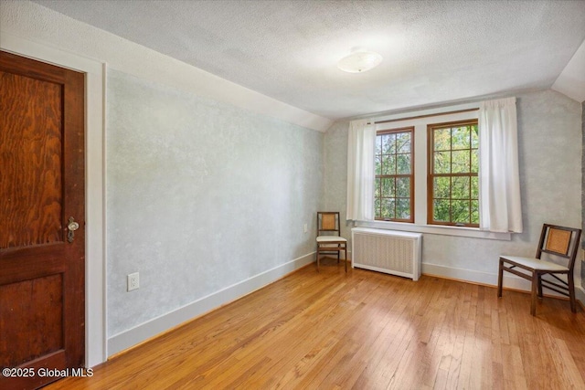 unfurnished room with radiator, lofted ceiling, light wood-style flooring, baseboards, and a textured ceiling
