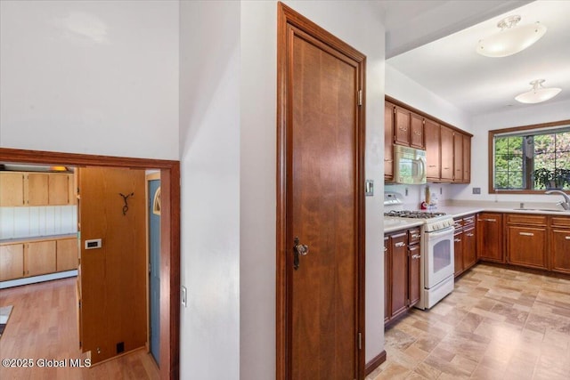 kitchen with white appliances, light countertops, brown cabinetry, and a sink