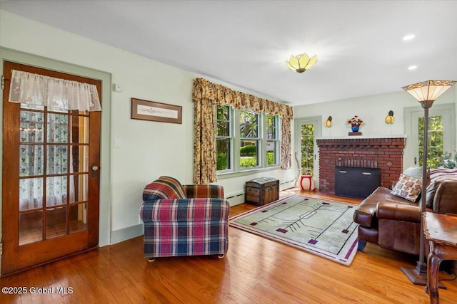 living room with a baseboard radiator, wood finished floors, plenty of natural light, a brick fireplace, and recessed lighting